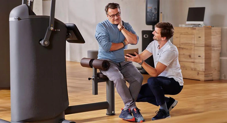 Trainer hilft beim Fitnessgerät.